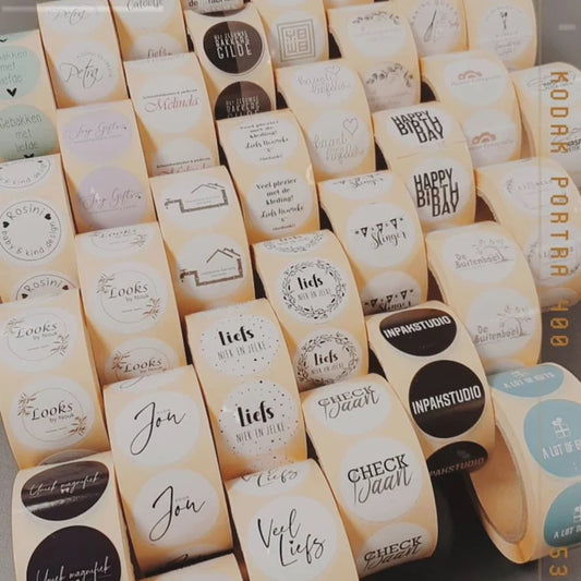 Voorbeeld van diverse rolstickers met gepersonaliseerde ontwerpen, zoals logo's, tekst en afbeeldingen. De stickers zijn verkrijgbaar in verschillende stijlen en vormen. - Liefs en Lintjes